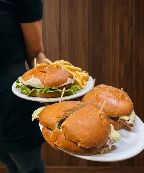 Moza llevando a la mesa dos platos con chivitos al pan y papas fritas